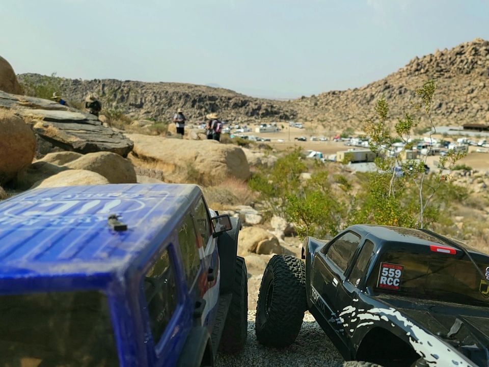 RC crawlers on desert boulders with more rigs in the canyon behind