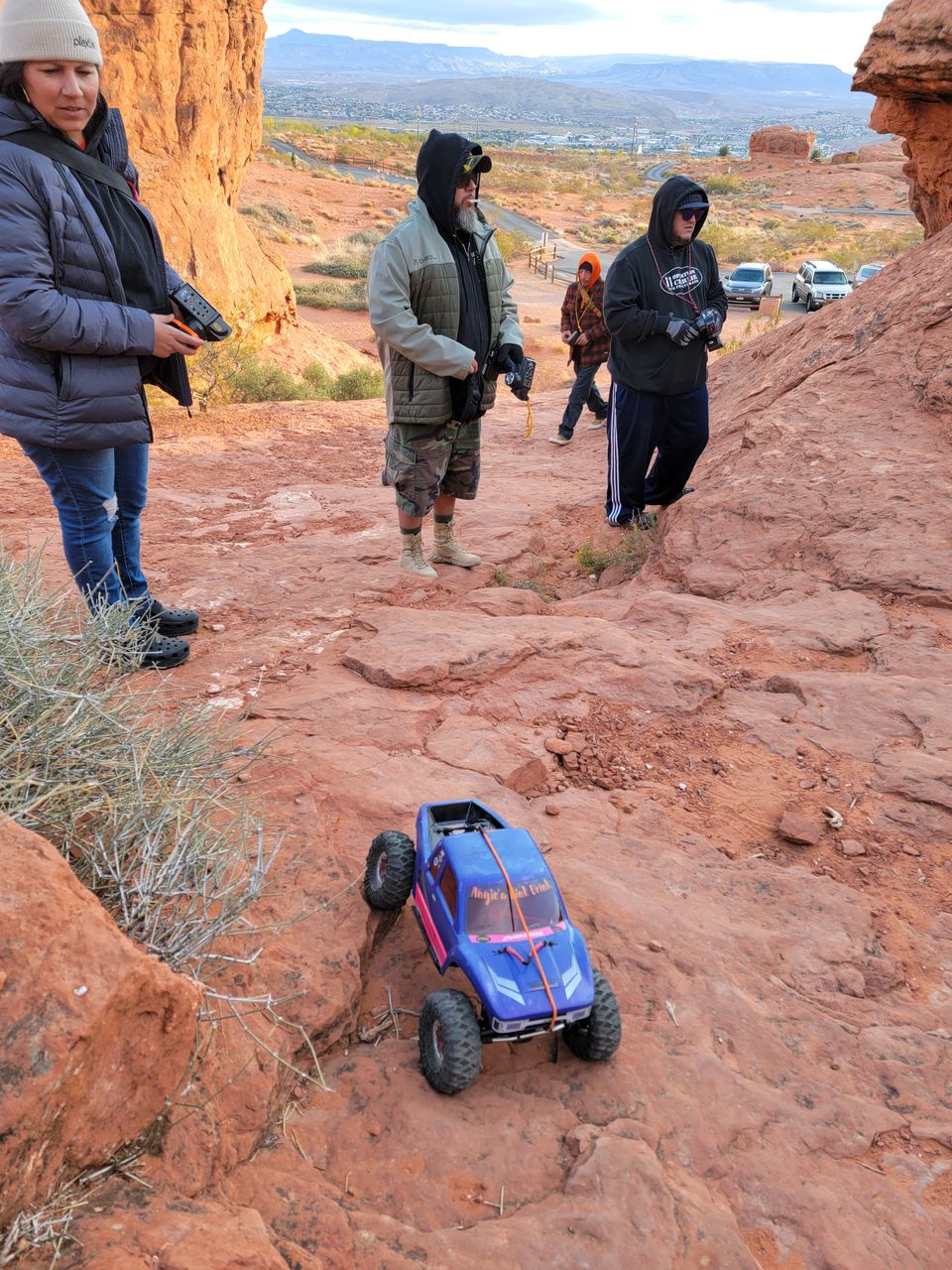 Members guiding a blue RC crawler down a red rock slope